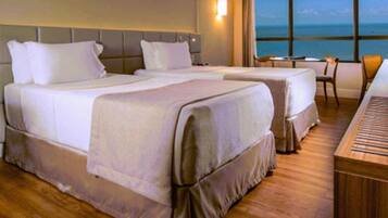 A hotel room with two beds, a piano, a small table, and a view of the ocean.