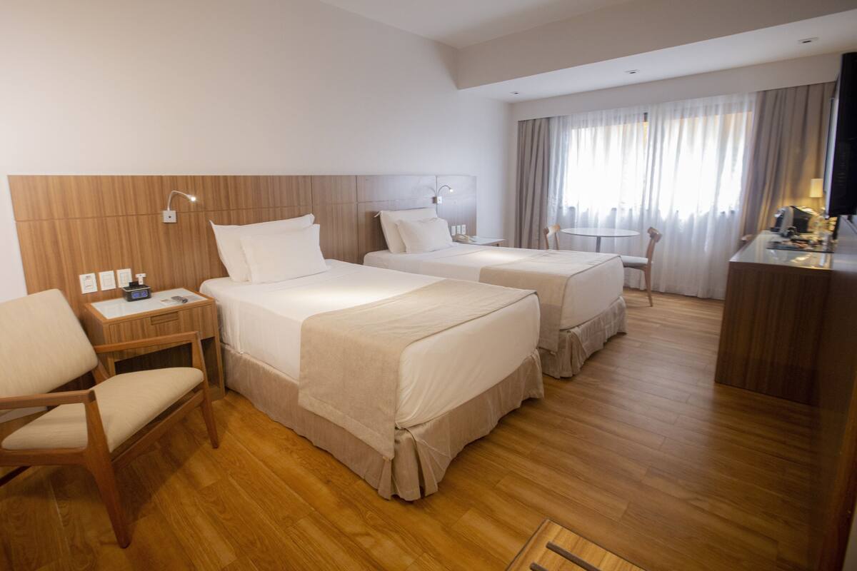 A hotel room with two beds, a desk with a chair, a small table, and a TV.