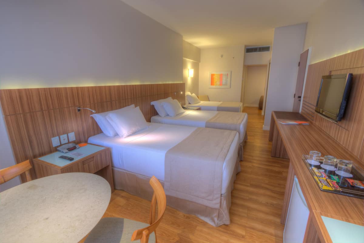 A hotel room with two beds, a desk, a chair, a TV, and a minibar.