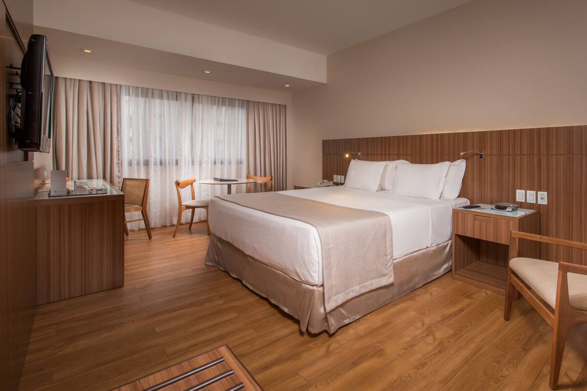 A hotel room with a large bed, a desk, a chair, and a television.