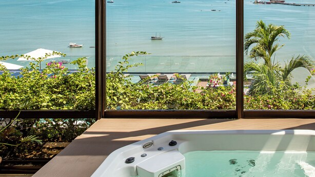 A view from a window of a hotel room with a large bathtub, a pool area, and a view of the ocean with boats. - Hotel Gran Marquise (Fortaleza)