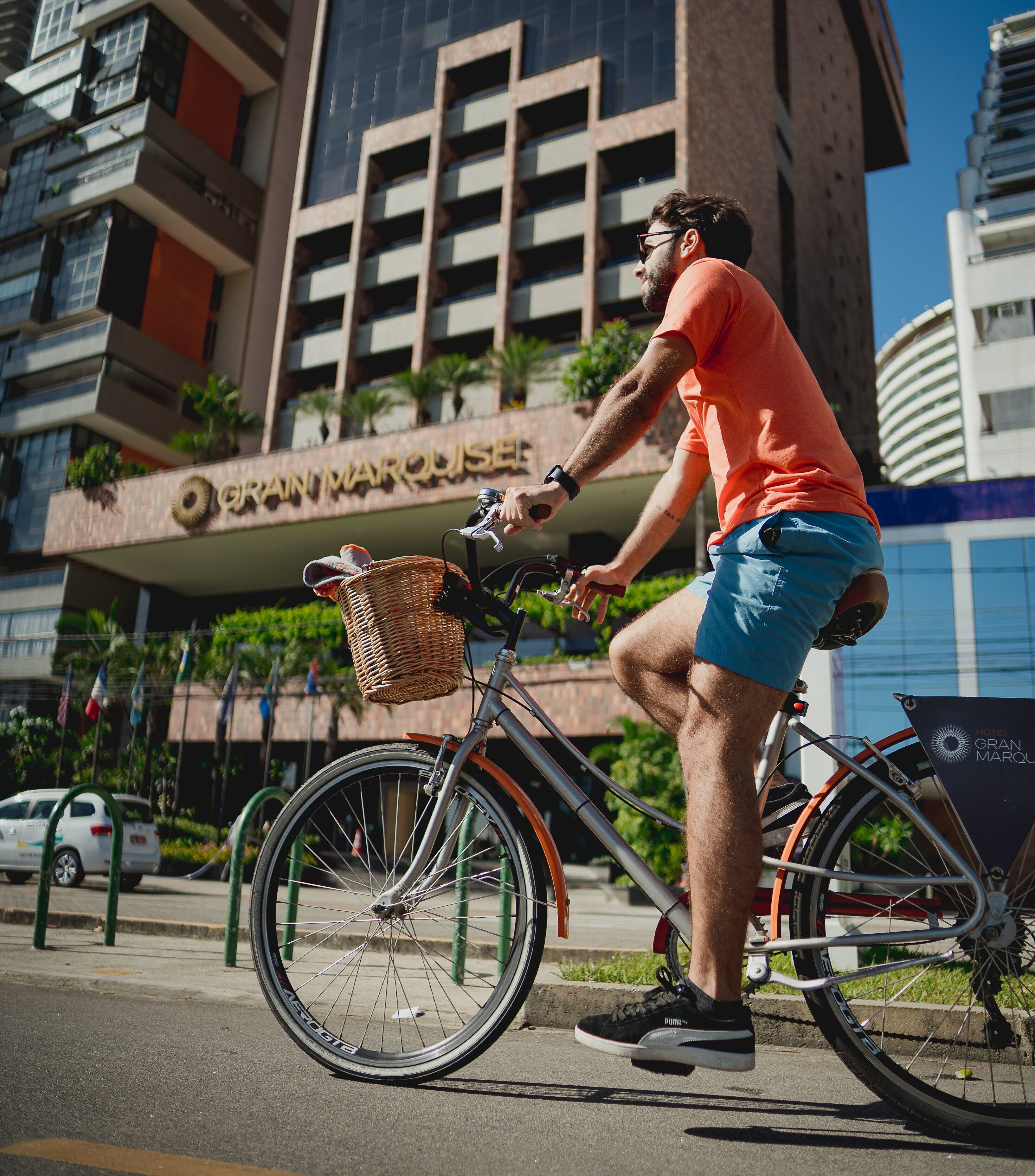 A person riding a bicycle with a basket in front of a building labeled "GRAN MARQUE."