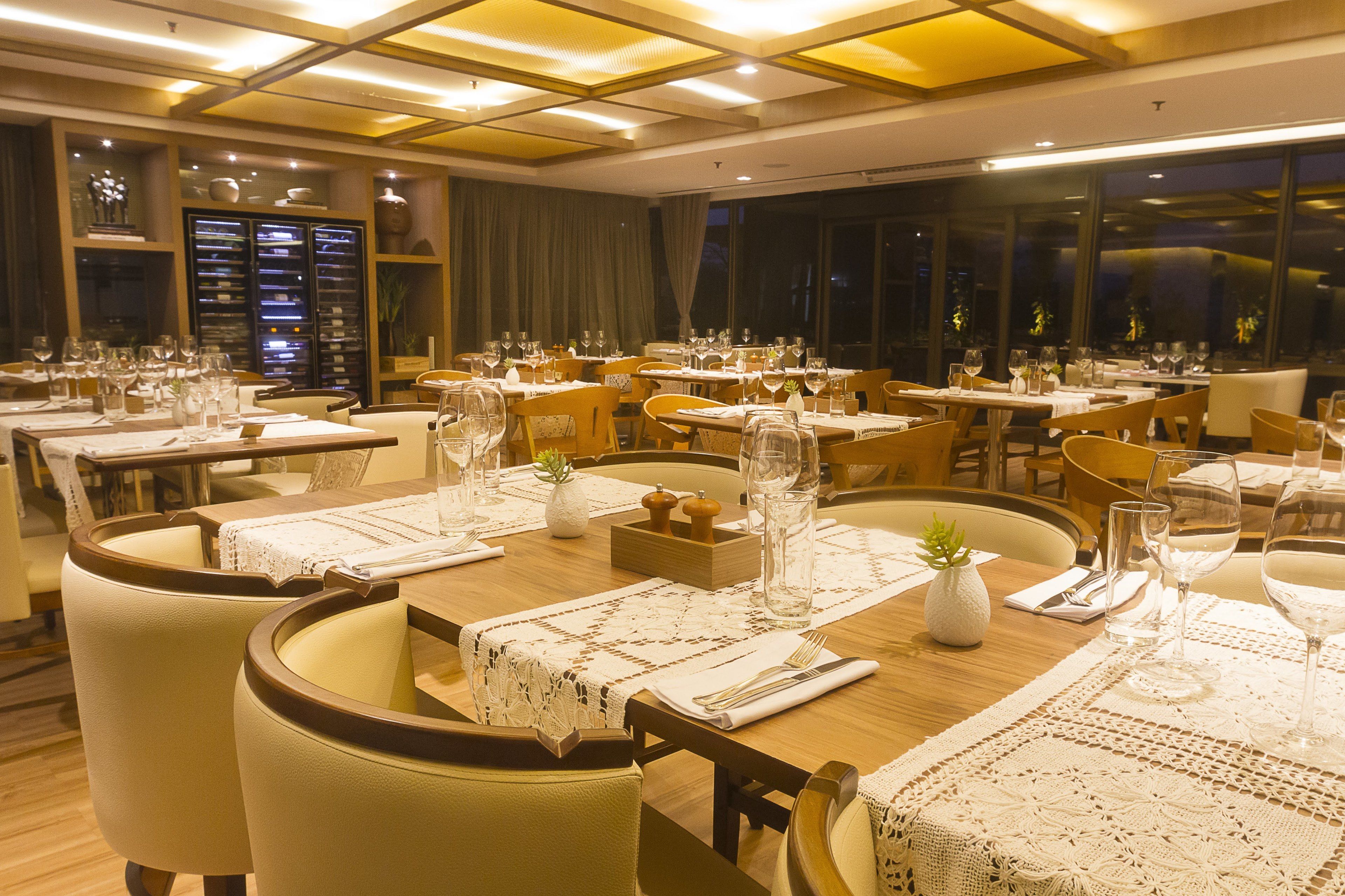 A restaurant with multiple dining tables set with white tablecloths, candles, and wine glasses.