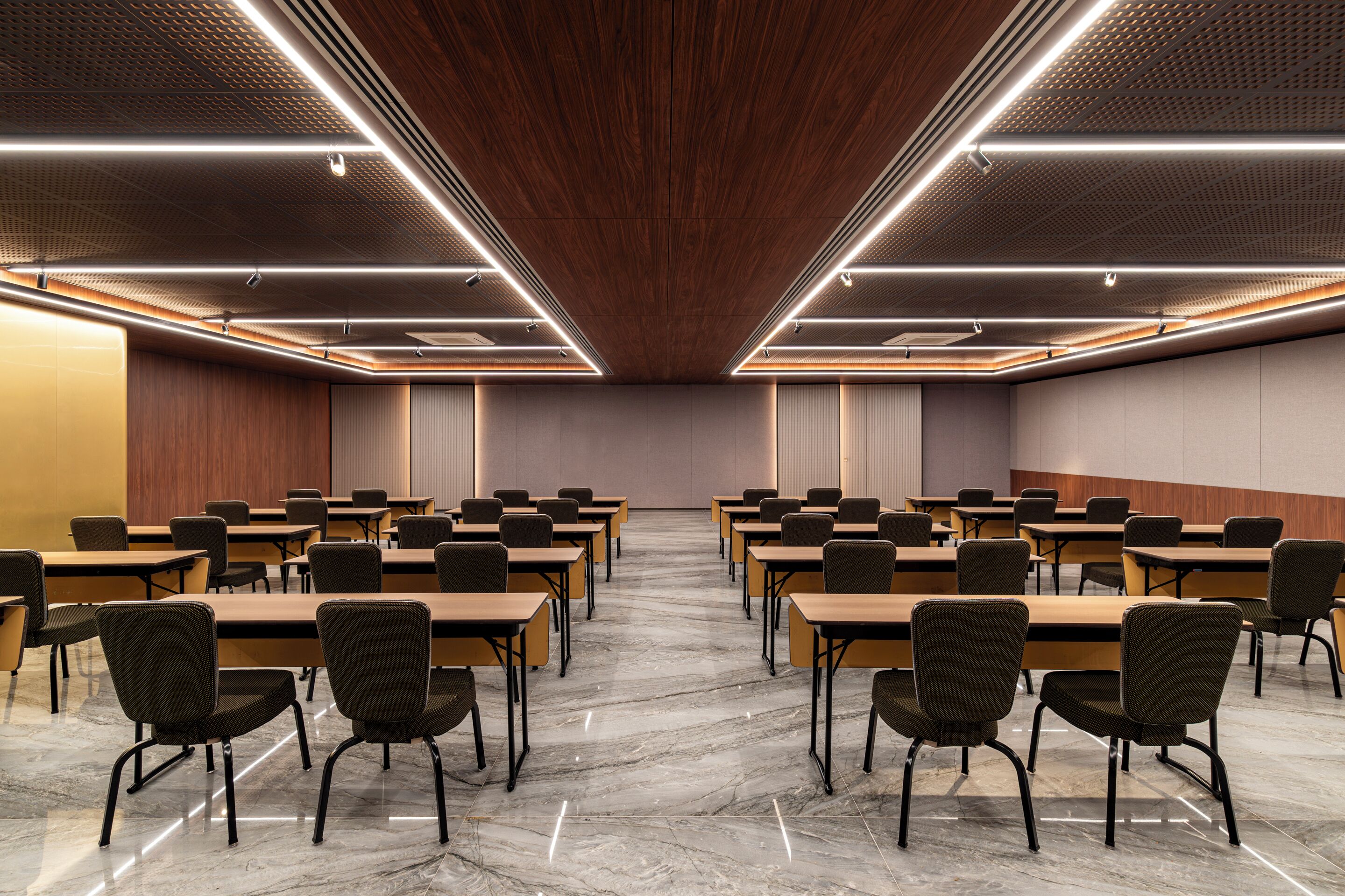 A conference room with rows of tables and chairs, wooden panel walls, and a polished marble floor.