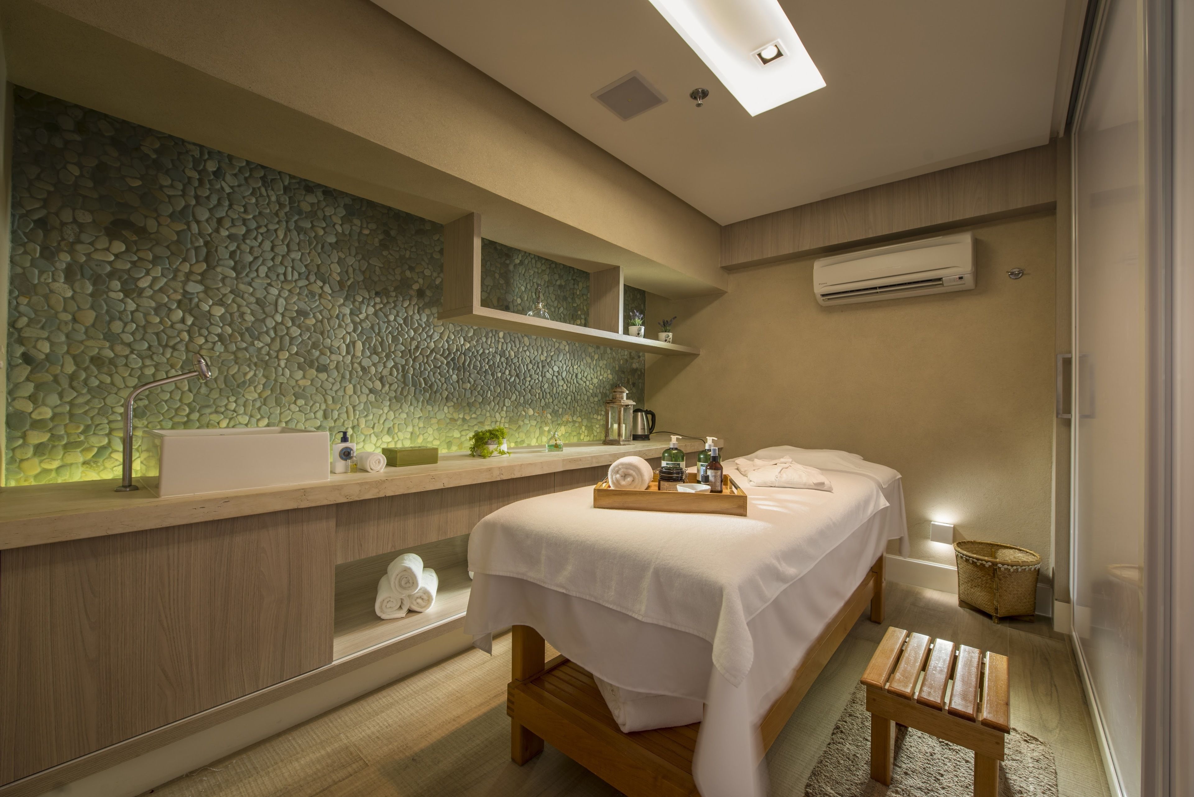 A modern bathroom with a stone wall, a wooden vanity, a bed, and a small wooden stool.