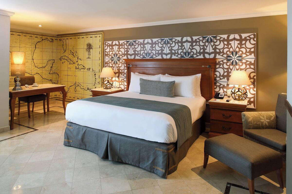Une chambre d’hôtel avec un grand lit, un bureau, deux chaises et une tête de lit décorative.