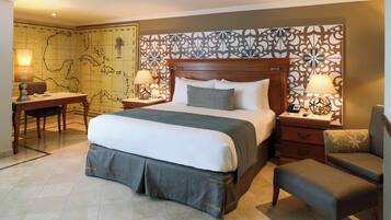 A hotel room with a large bed, a desk, two chairs, and a decorative headboard.