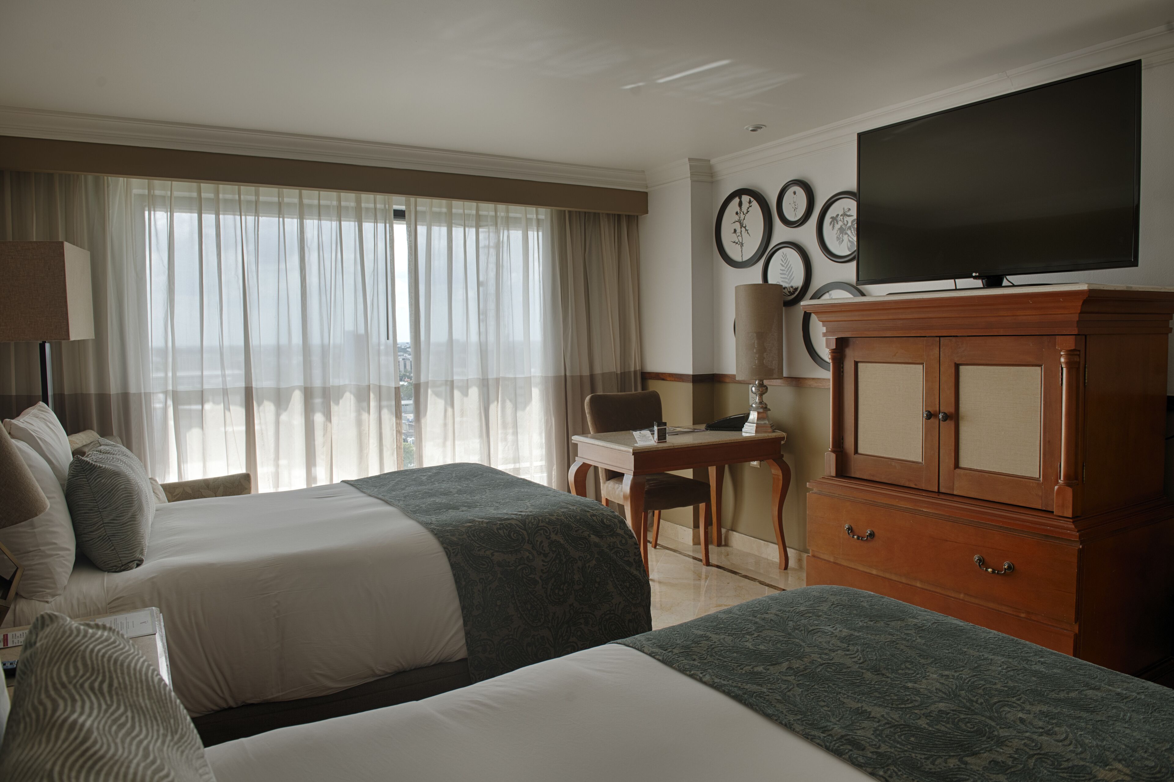 A hotel room with two beds, a desk, a television, and a cabinet.
