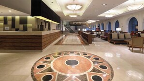 A hotel lobby with a reception desk, seating area, and a staircase leading to upper floors.