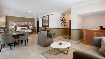 A hotel room with a bed, a dining area with a table and chairs, a sofa, a coffee table, and a decorative wall with circular patterns.