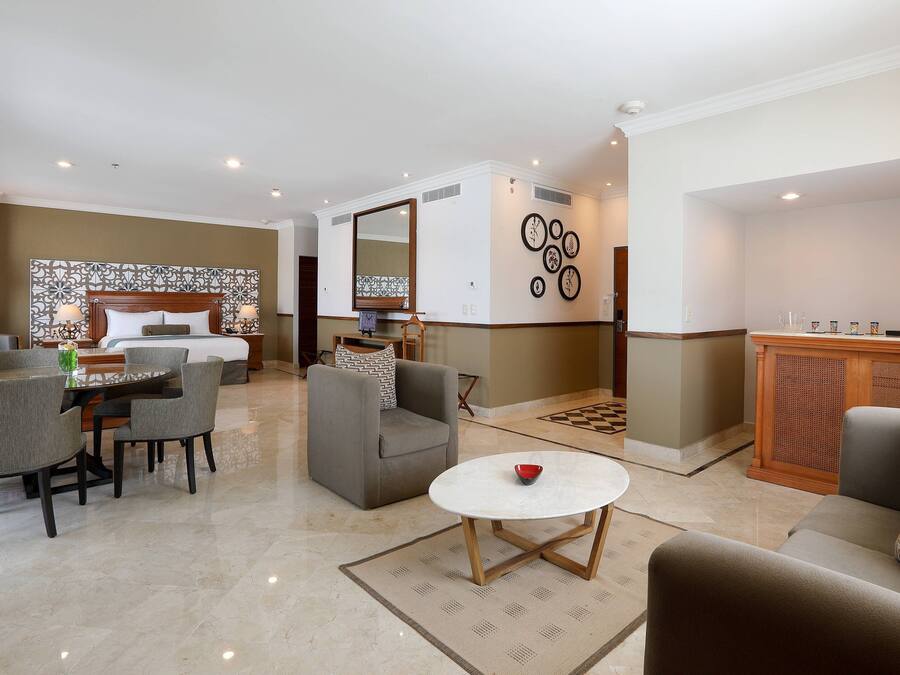 A hotel room with a bed, a dining area with a table and chairs, a sofa, a coffee table, and a decorative wall with circular patterns.