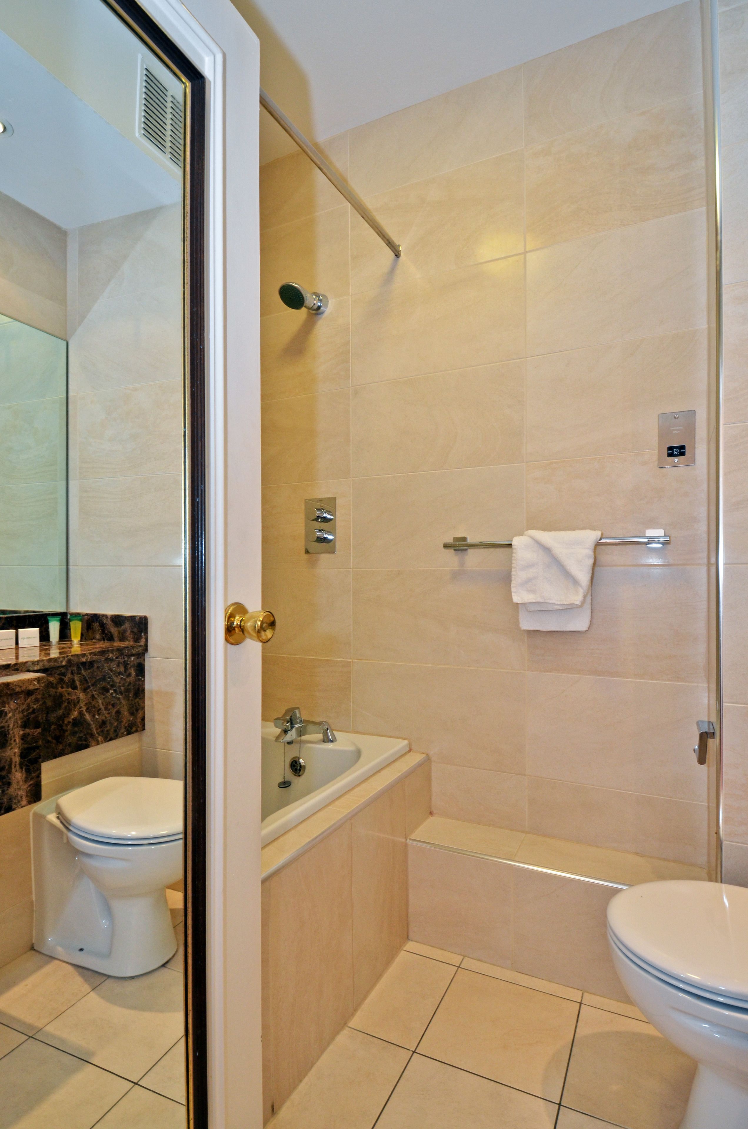 Une salle de bain avec une douche à porte en verre, un lavabo et deux toilettes.