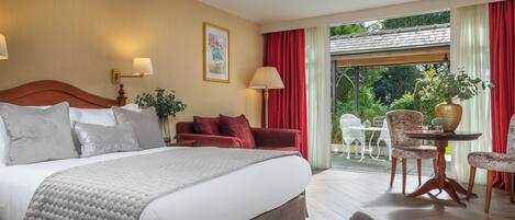 Habitación de hotel con una cama grande, una zona de comedor con mesa y sillas, y un balcón con vistas al exterior.