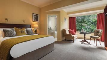 Habitación de hotel con una cama grande, un área de descanso con una mesa y vistas a zonas verdes por la ventana.