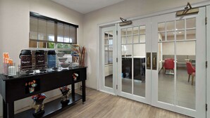 A room with a black console table displaying coffee and tea options, a large window, and a sliding glass door leading to a dining area with red chairs. - Comfort Inn & Suites Santee (Santee)