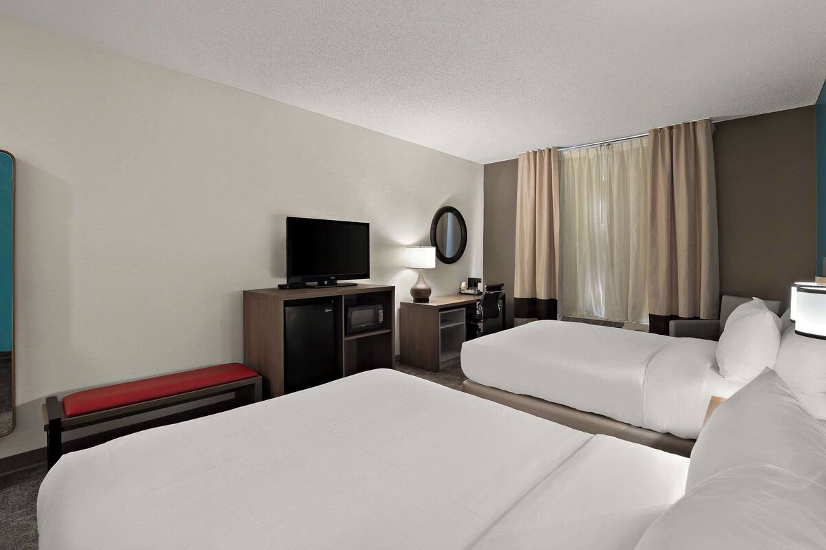 Habitación de hotel con dos camas, un televisor, un escritorio con lámpara y un espejo.