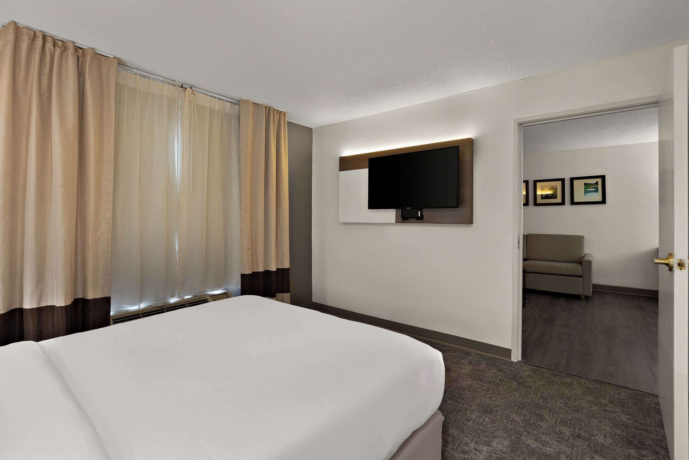 Une chambre d’hôtel avec un lit, un téléviseur fixé au mur et une porte donnant sur une autre pièce.