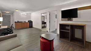 A modern living room with a sofa, a red ottoman, a TV mounted on the wall, and a wooden entertainment unit. - Comfort Inn & Suites Santee (Santee)