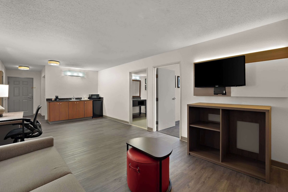 Una sala de estar moderna con un sofá, un reposapiés rojo, un televisor montado en la pared y un mueble de madera para entretenimiento.