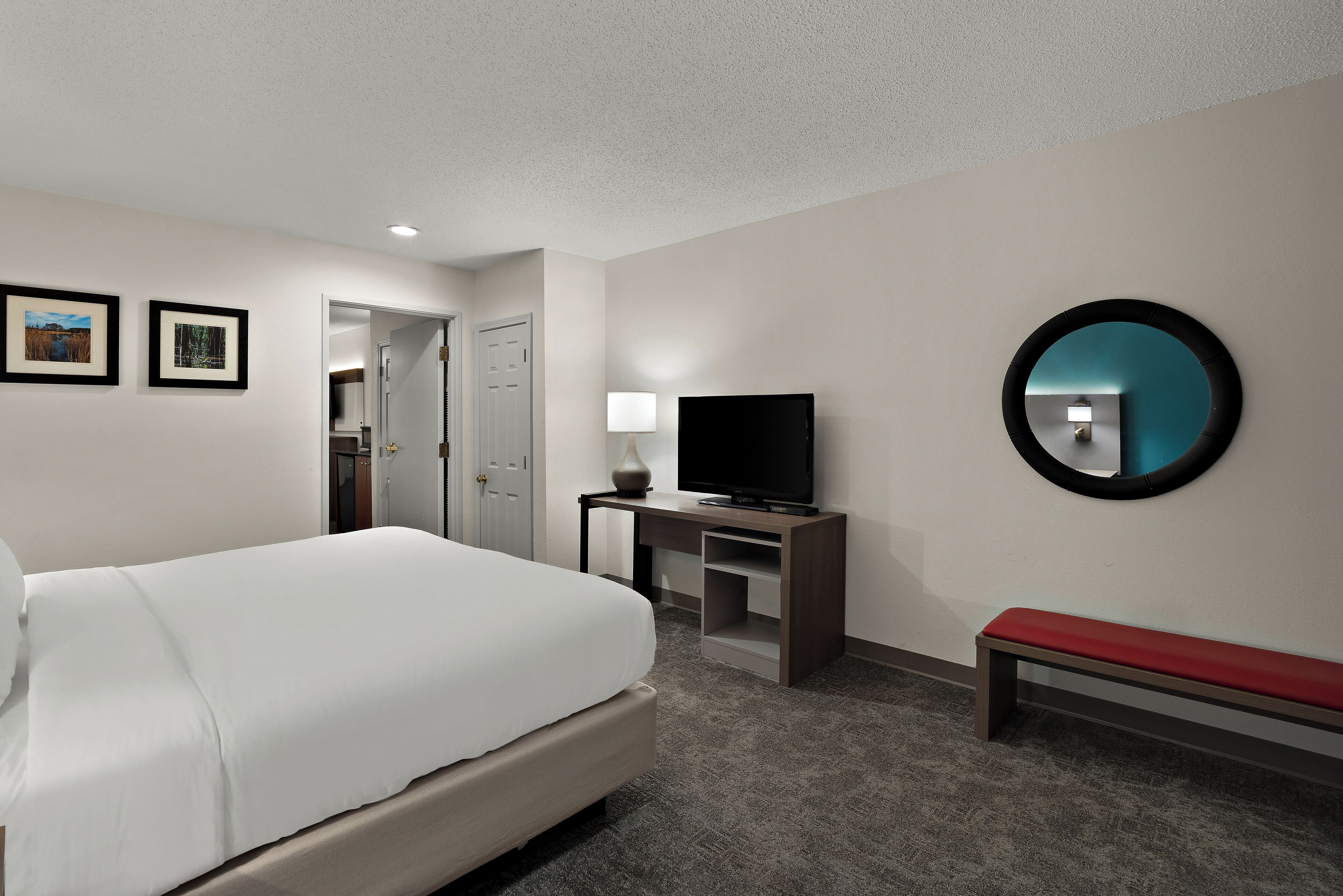 A hotel room with a bed, a TV, a desk, a bench, and a mirror.