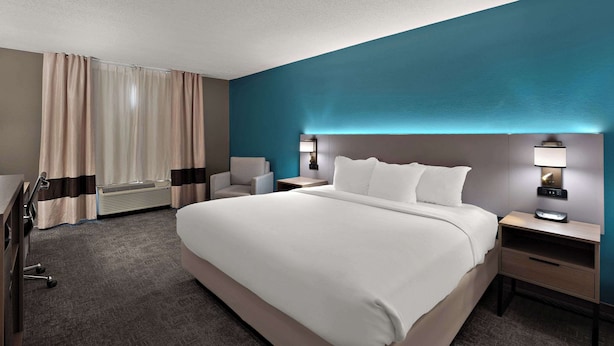 A hotel room with a large bed, a desk, a chair, a desk lamp, and a wall-mounted lamp. - Comfort Inn & Suites Santee (Santee)