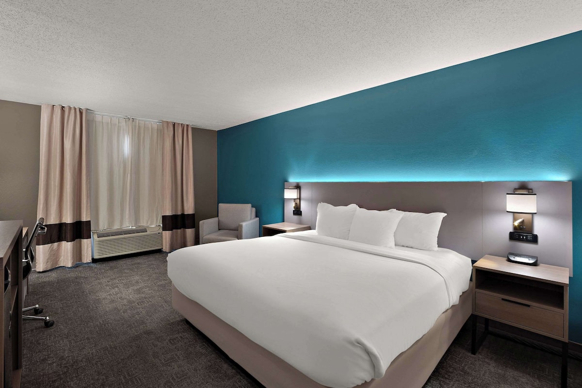 Una habitación de hotel con una cama grande, un escritorio, una silla, una lámpara de escritorio y una lámpara de pared.