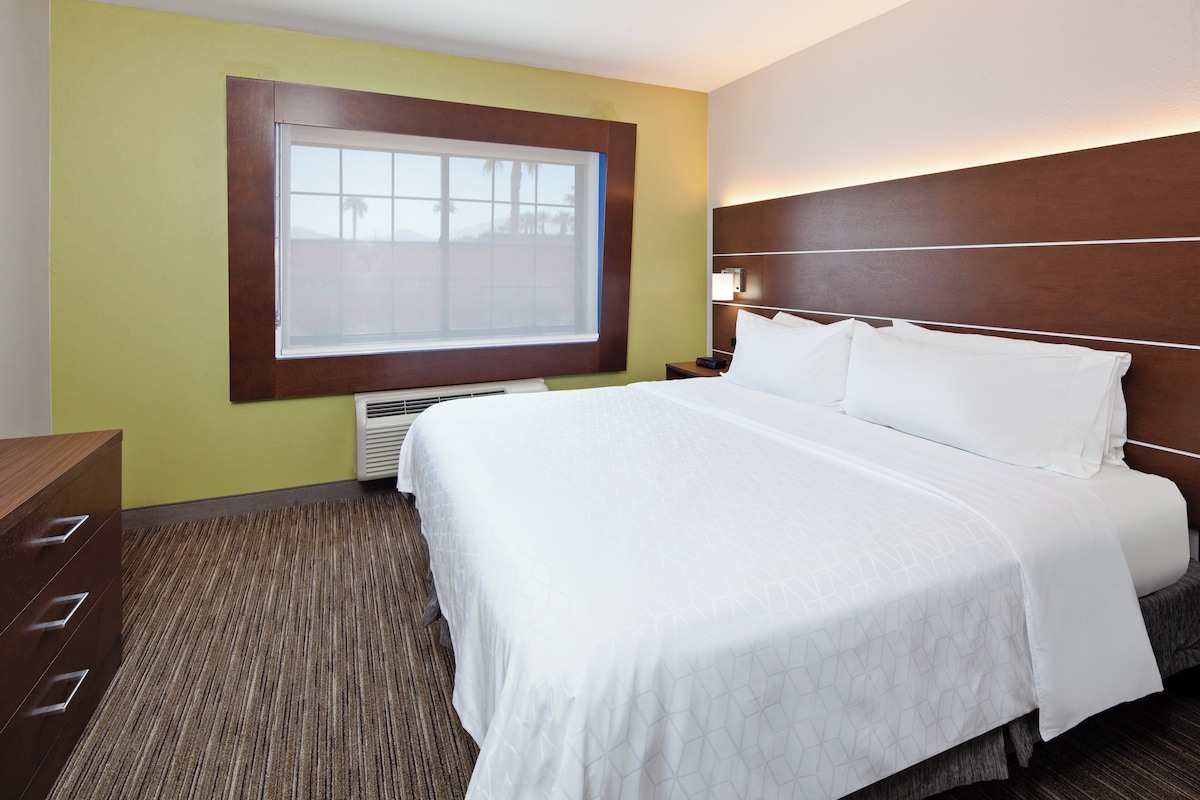 Une chambre d’hôtel comprenant un lit, une table de chevet, une commode, une fenêtre et un appareil de climatisation.