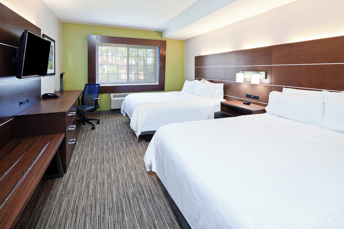 Une chambre d’hôtel avec deux lits, un bureau, une chaise, une télévision et une fenêtre.
