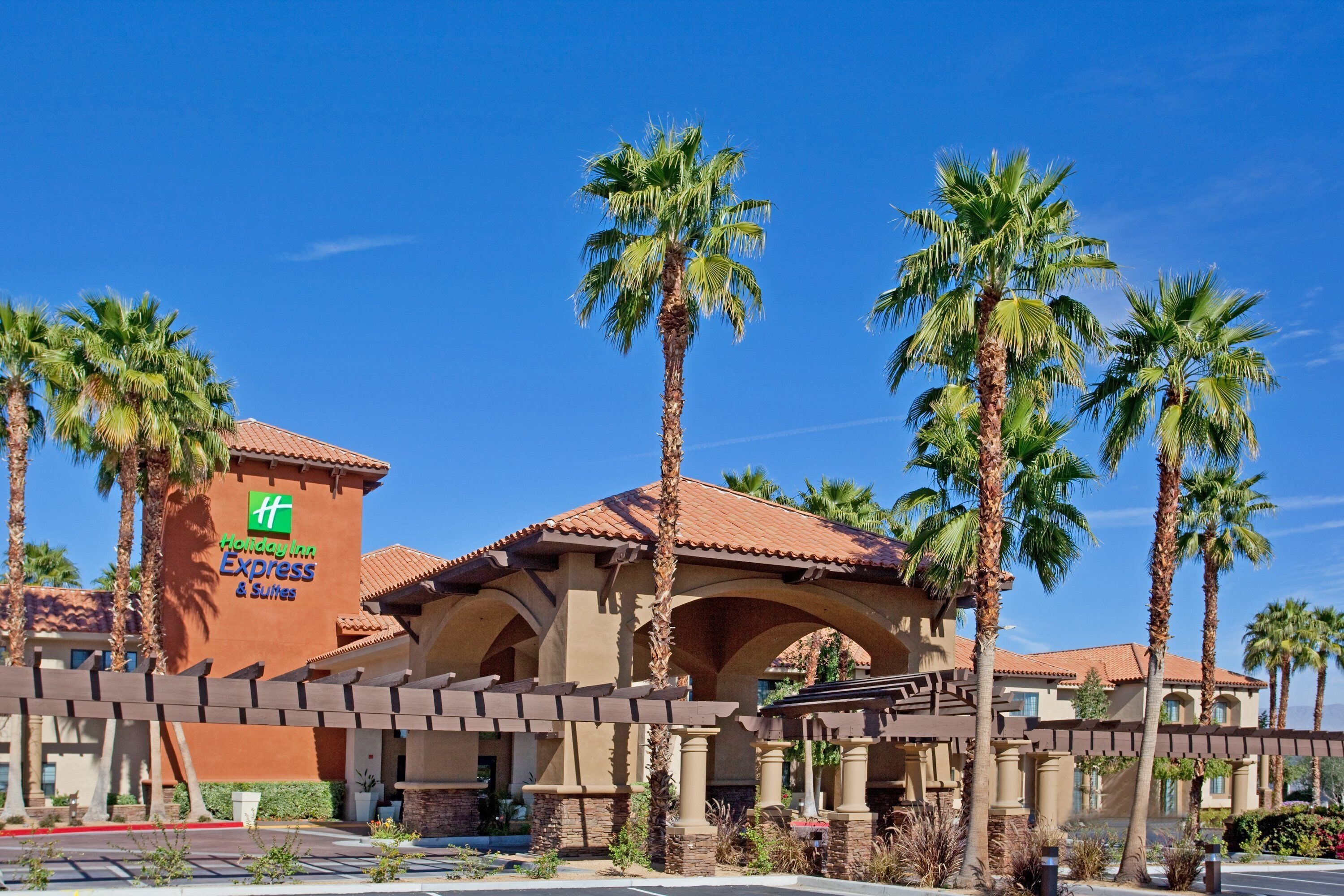 A Holiday Inn Express & Suites building with a red-tiled roof, palm trees, and a clear blue sky.