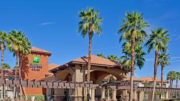 A Holiday Inn Express & Suites building with a red-tiled roof, palm trees, and a clear blue sky.