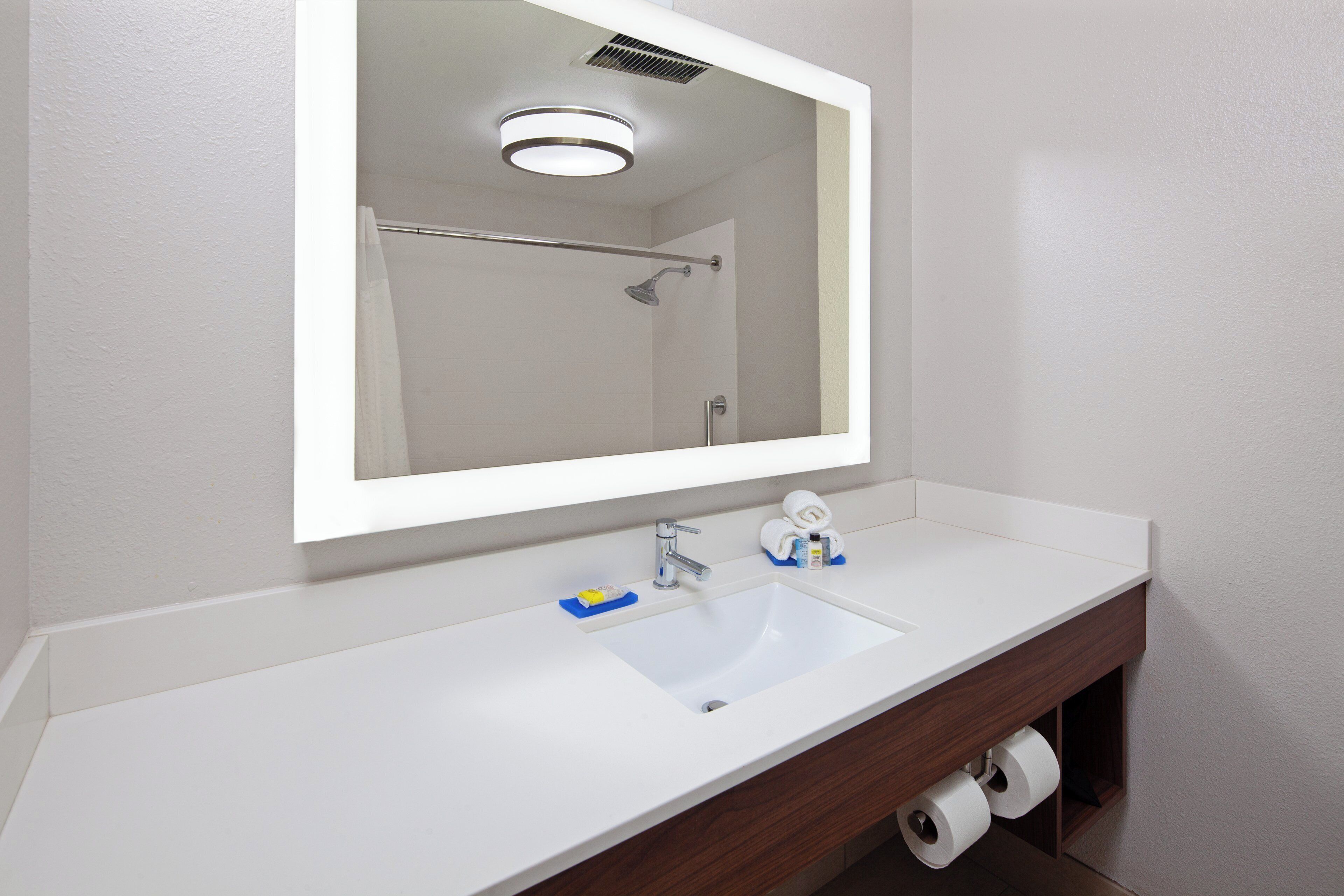 A bathroom with a white sink, a mirror, and a shower visible in the reflection.