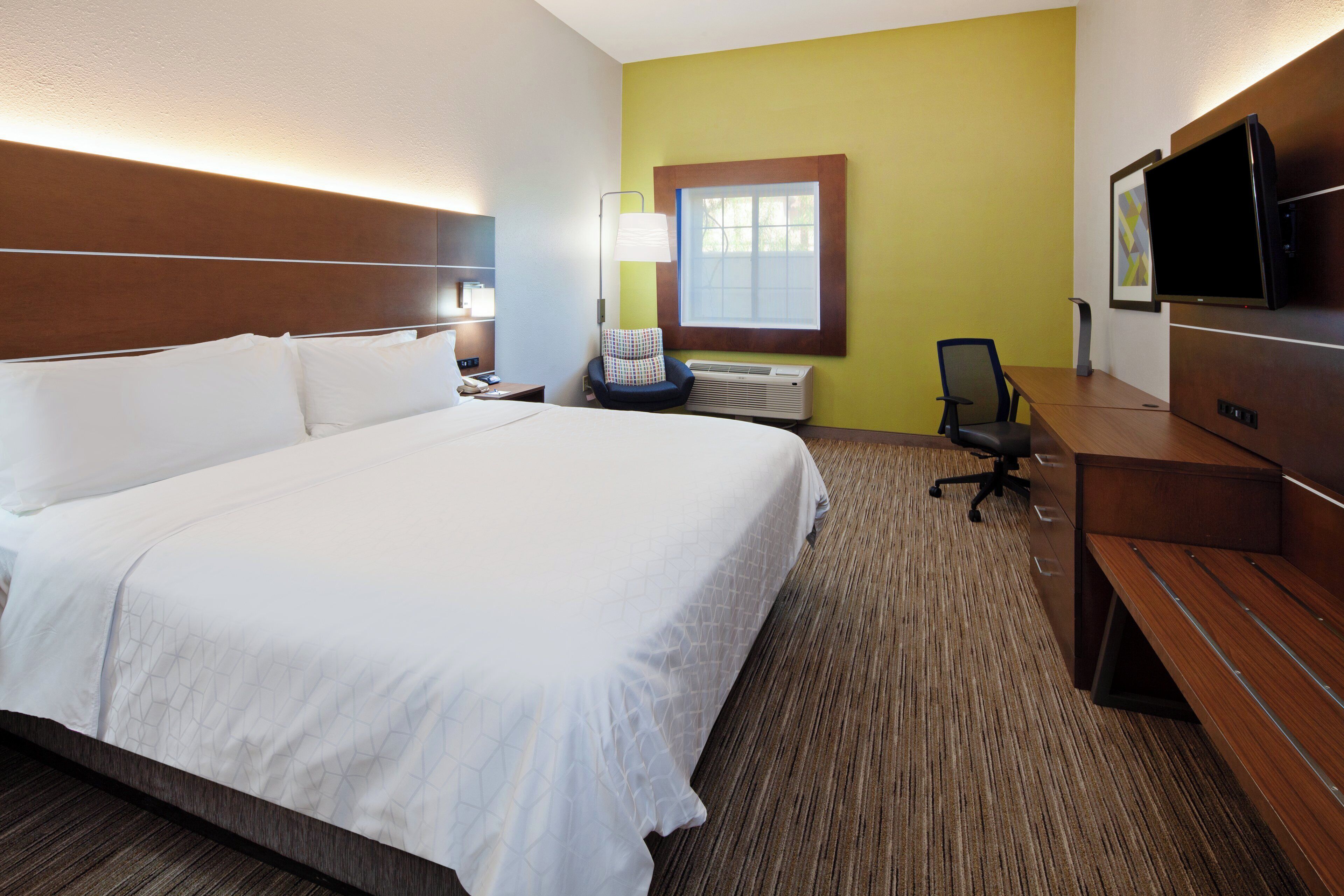 A hotel room with a large bed, a desk, a chair, a television, and a window.