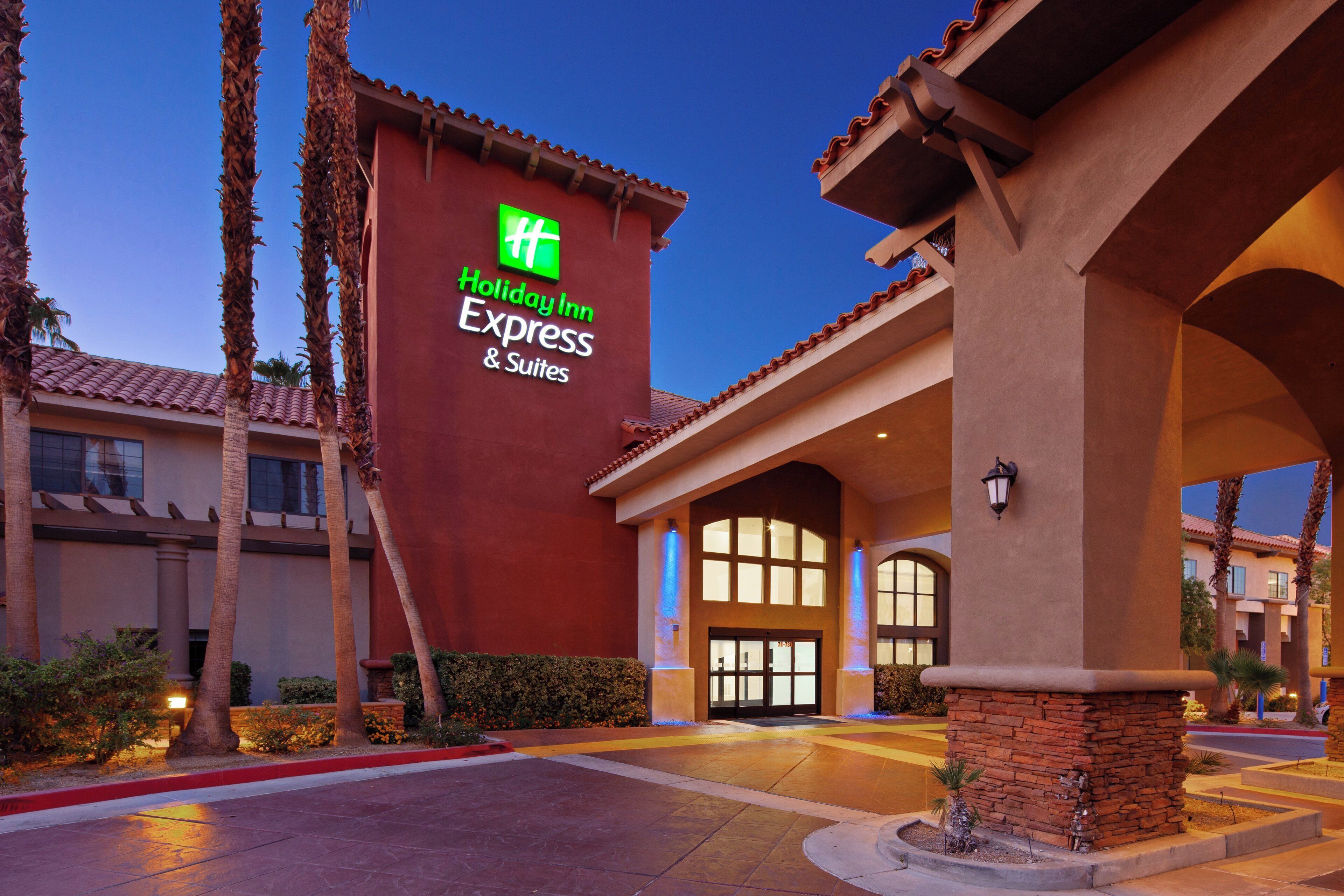 A Holiday Inn Express & Suites building with a red facade, large windows, and palm trees.