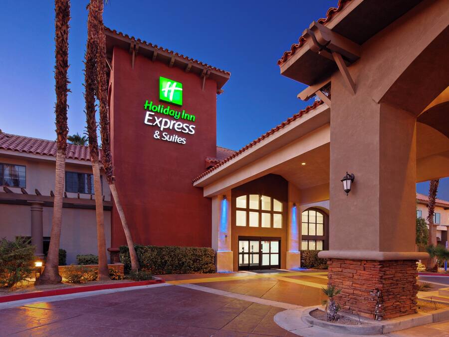Edifici d'Holiday Inn Express & Suites amb façana vermella, grans finestres i palmeres.