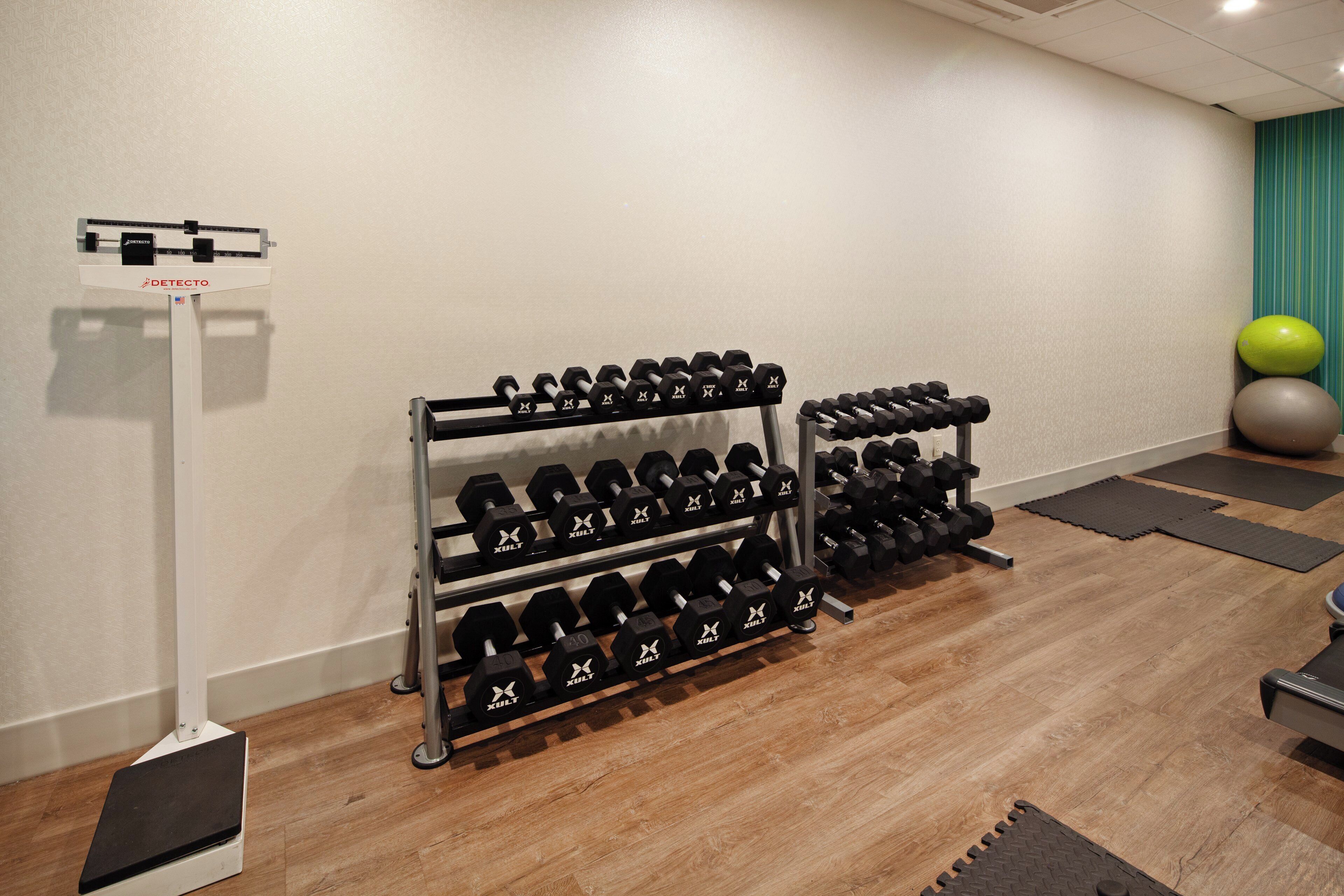 Une salle de sport équipée de plusieurs jeux d’haltères, de ballons d’exercice et d’une balance.