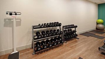 A gym with multiple sets of dumbbells, exercise balls, and a weight scale.