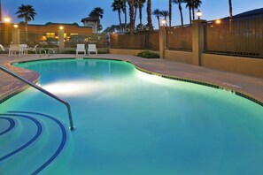 A swimming pool with a tiled edge, a metal ladder, and a few lounge chairs.