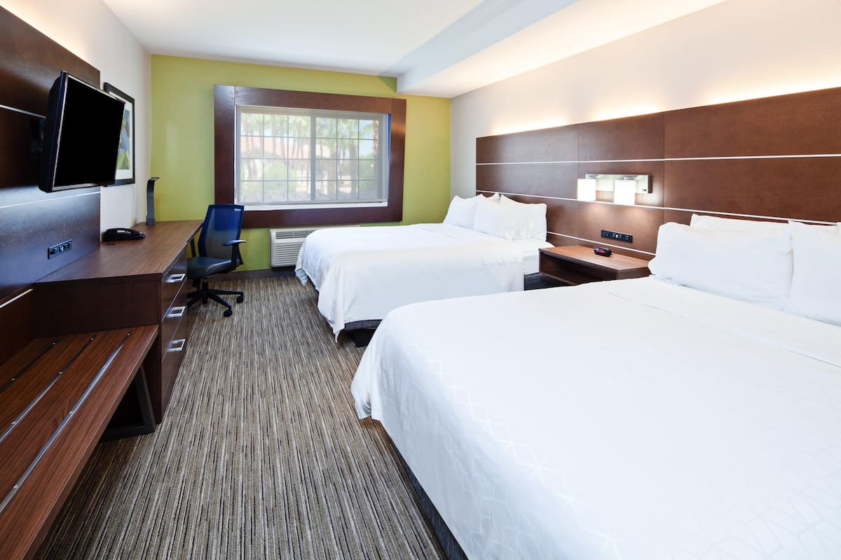 Habitación de hotel con dos camas, un escritorio con silla, televisor y ventana con persianas.