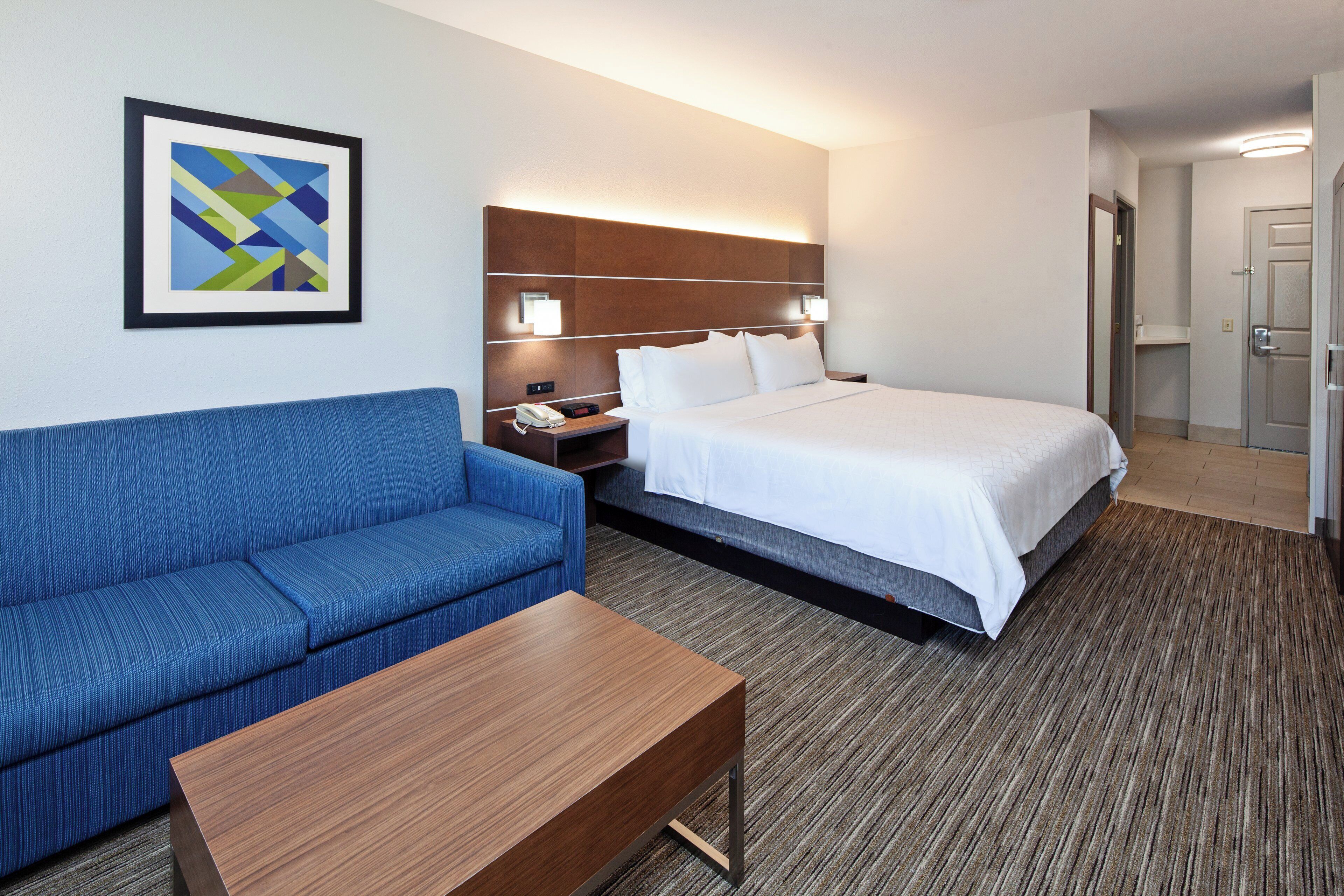 Ein Hotelzimmer mit einem Bett, einem blauen Sofa, einem Holztisch und einem an der Wand befestigten Telefon.