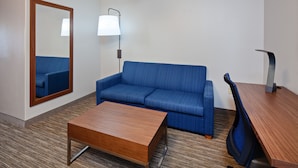 A hotel room with a blue sofa, a wooden coffee table, a desk, and a lamp. - Holiday Inn Express & Suites Rancho Mirage - Palm Spgs Area by IHG (Rancho Mirage)