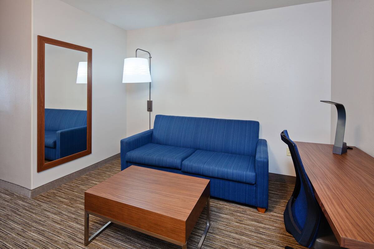 Habitación de hotel con un sofá azul, una mesa de centro de madera, un escritorio y una lámpara.