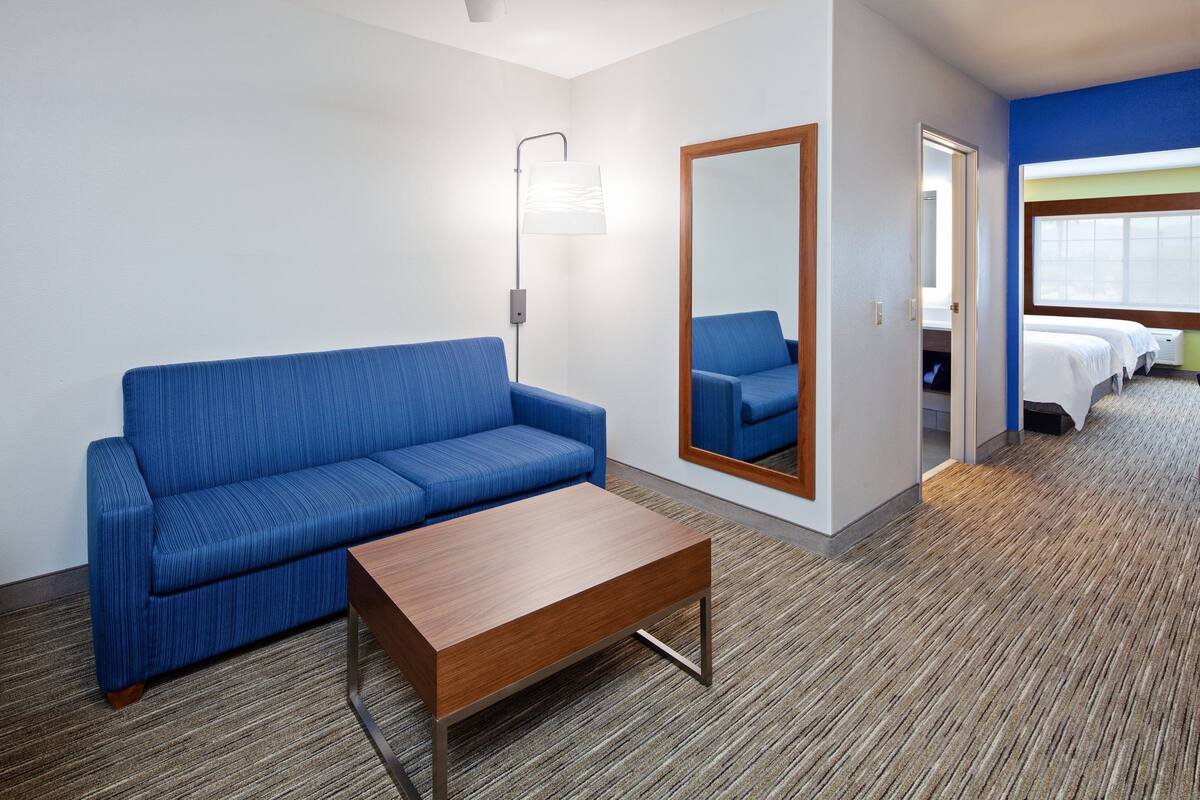 Una habitación de hotel con un sofá azul, una mesa de centro de madera, un espejo y una cama con cabecero azul.