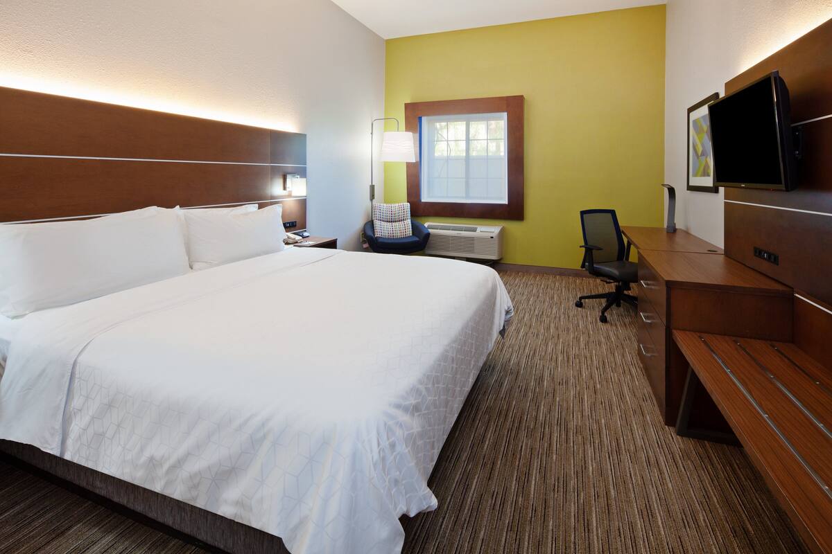 Habitación de hotel con una cama grande, un escritorio con silla, televisión y ventana con persianas.