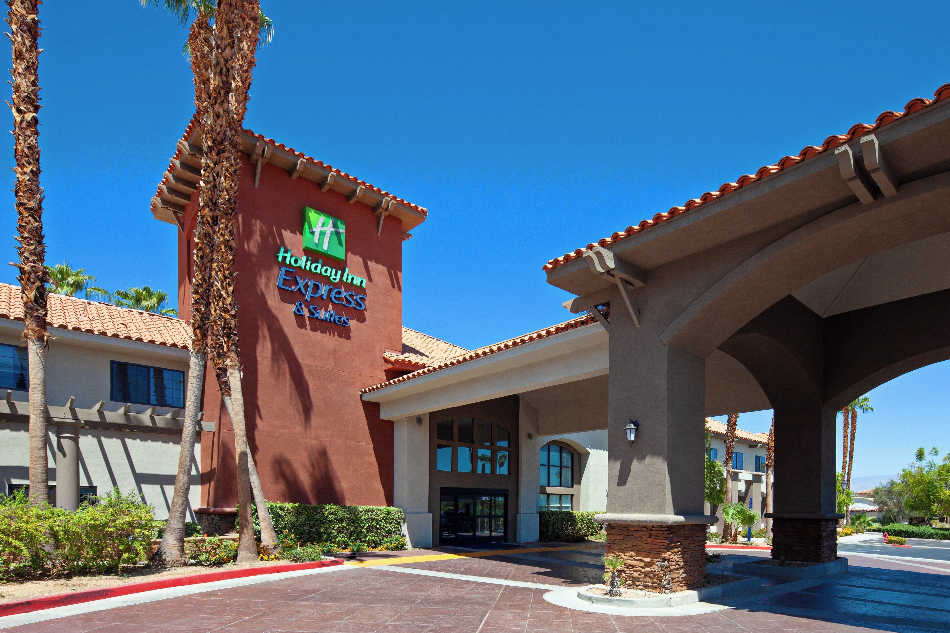 A Holiday Inn Express & Suites building with a clear blue sky, palm trees, and a red-tiled roof.