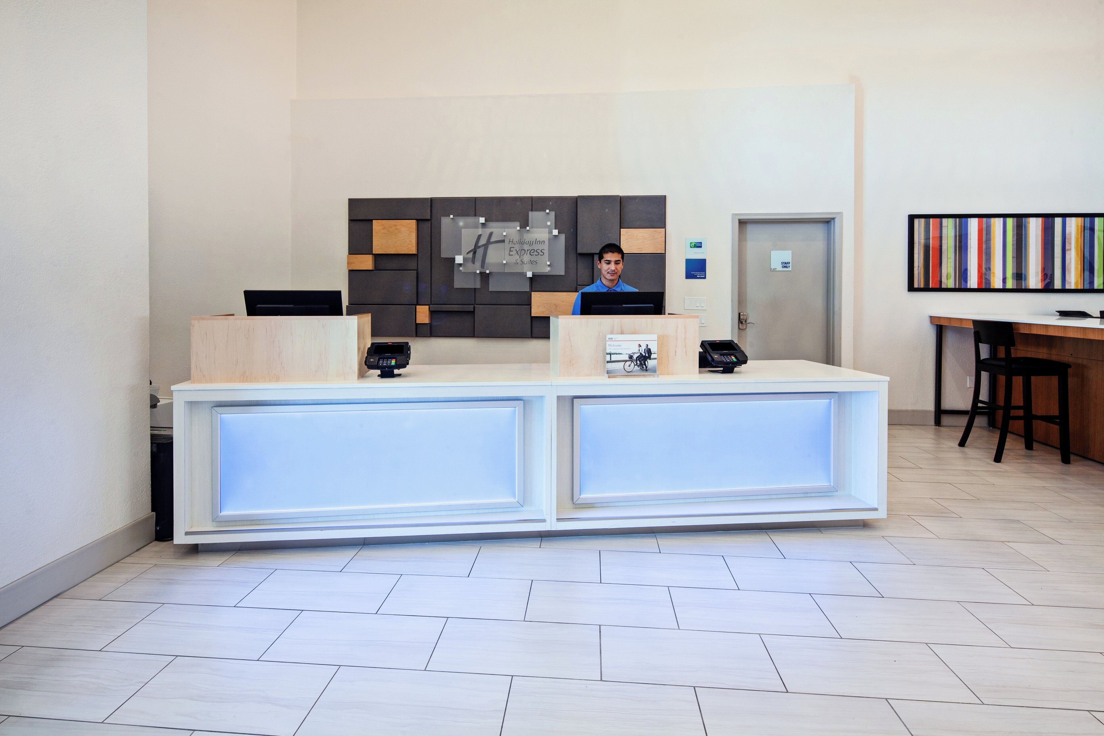A hotel reception desk with a modern design, a digital display, and a staff-only door.