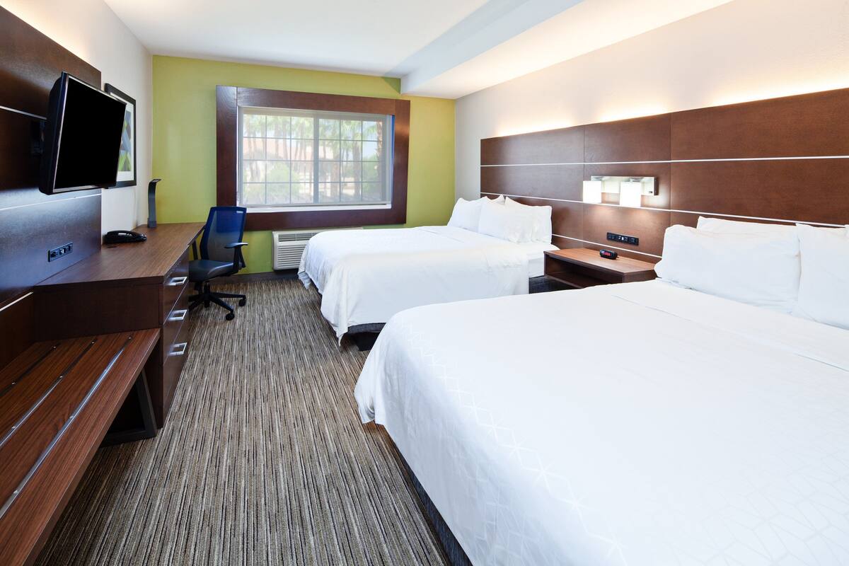 Habitación de hotel con dos camas, un escritorio con computadora, televisión y ventana con persianas.