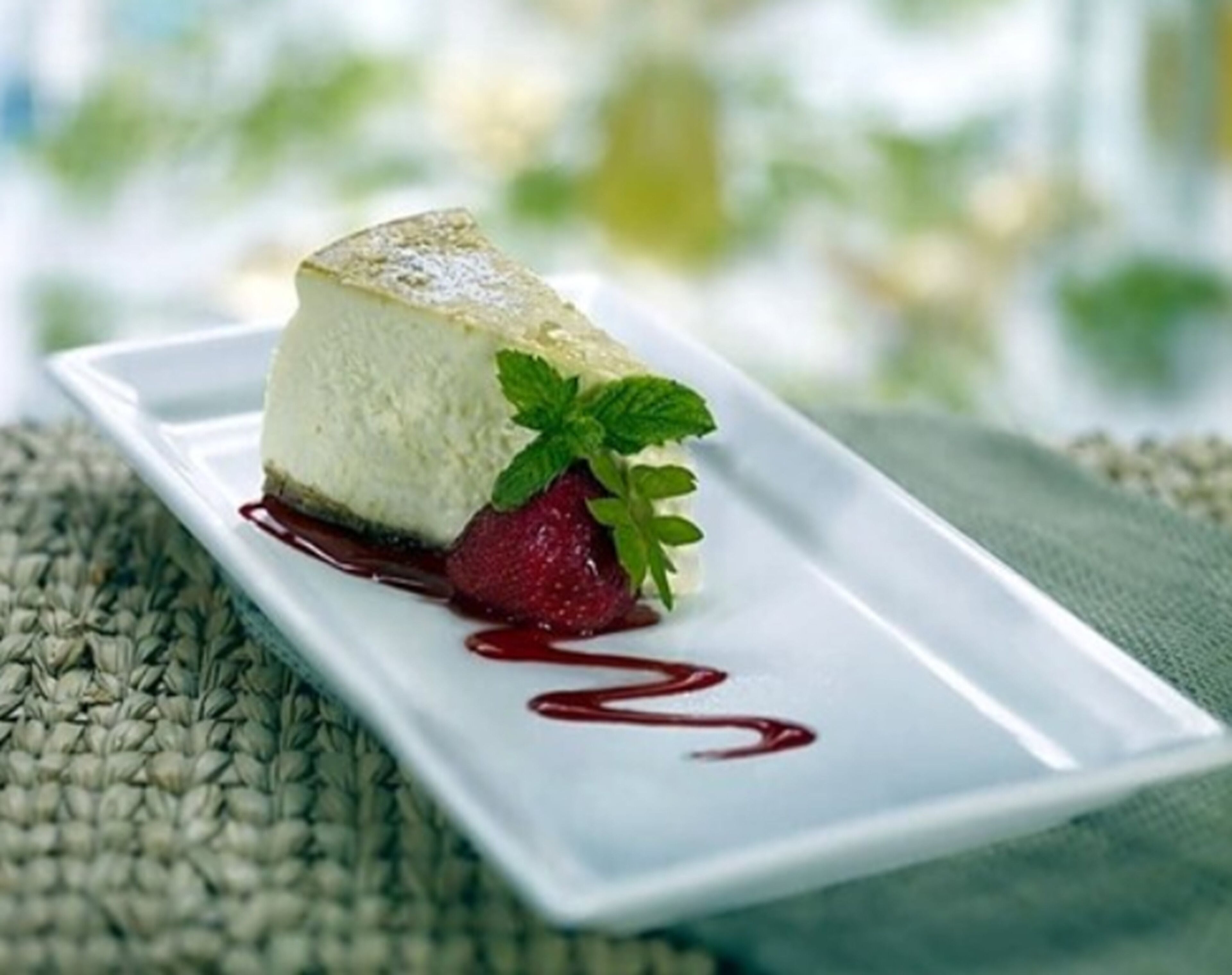 Een dessert op een wit bord, versierd met aardbei en munt, vergezeld van rode saus.
