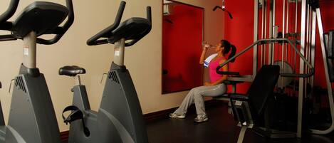 A gym with stationary bikes, a weight machine, and a red wall.