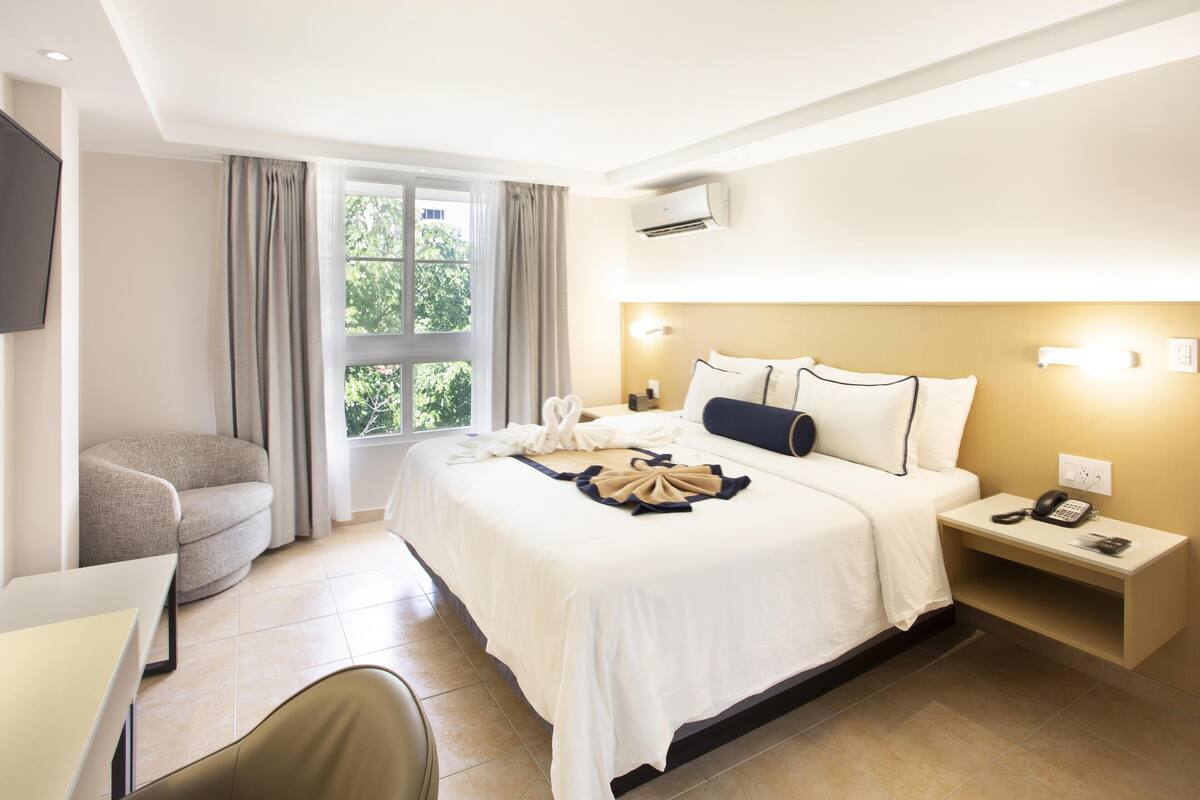 A hotel room with a bed, bedside table, chair, and a desk.
