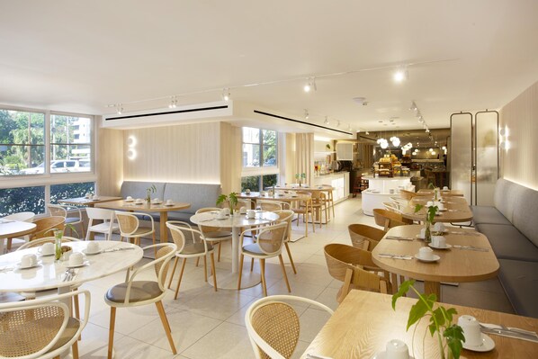 Un comedor moderno con mesas redondas y sillas de mimbre, que ofrece vistas de la ciudad a través de amplios ventanales.